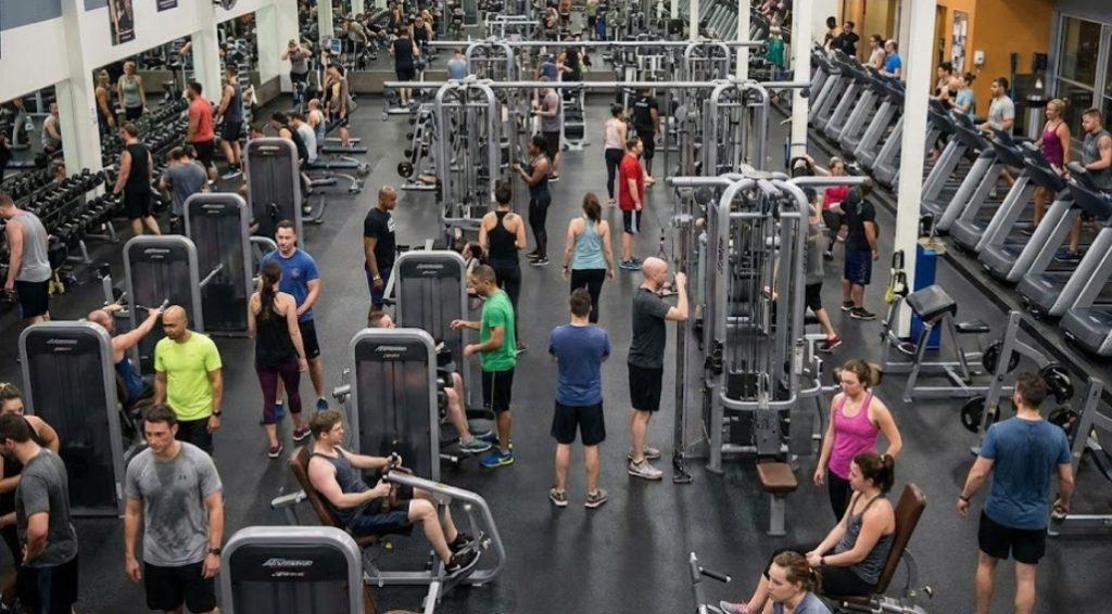 多くの人々で混雑している広々としたフィットネスジムの俯瞰写真。トレーニングマシン、フリーウェイト、有酸素運動エリアで多数の利用者が運動しており、活気がある様子。
